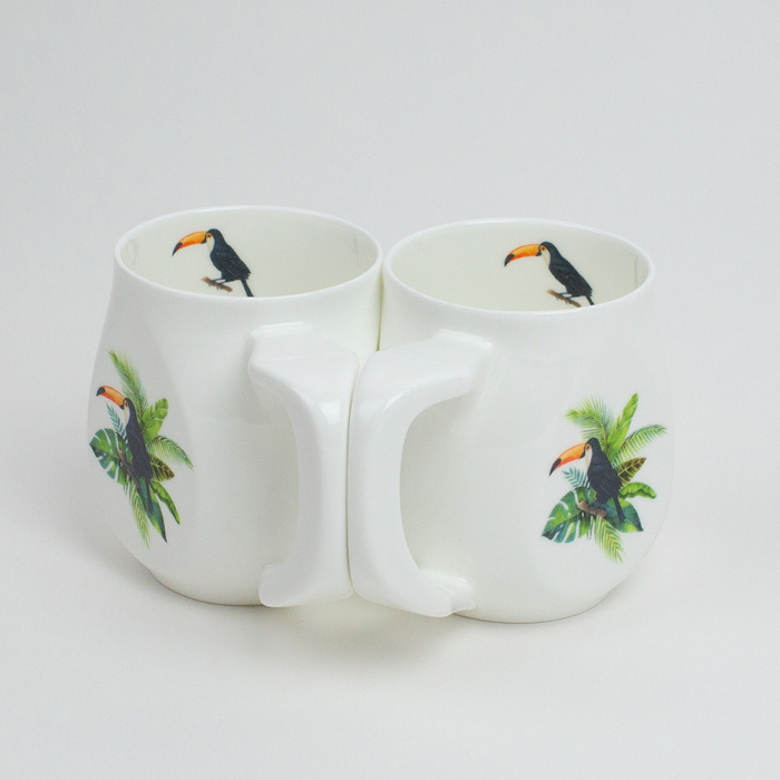 A pair of white fine bone china mugs with a colourful toucan printed on the side.